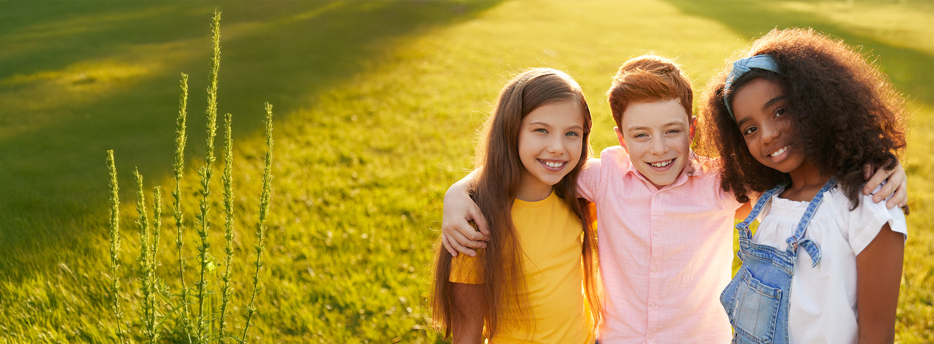 The image shows three young individuals posing together outdoors during daylight they are smiling and appear to be enjoying themselves.