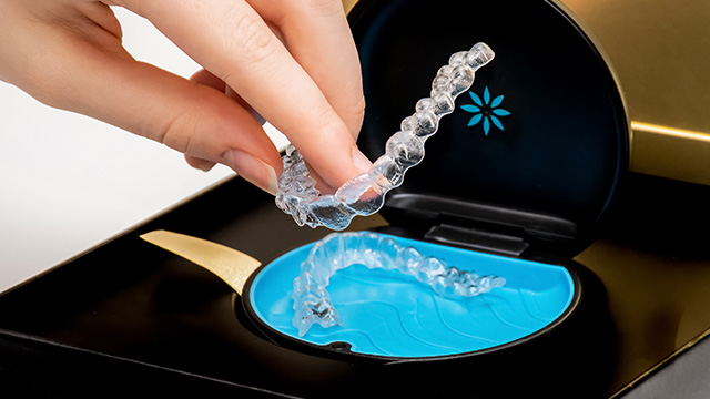 The image shows a hand holding a clear plastic tray with a blue substance inside, which appears to be a dental impression material.